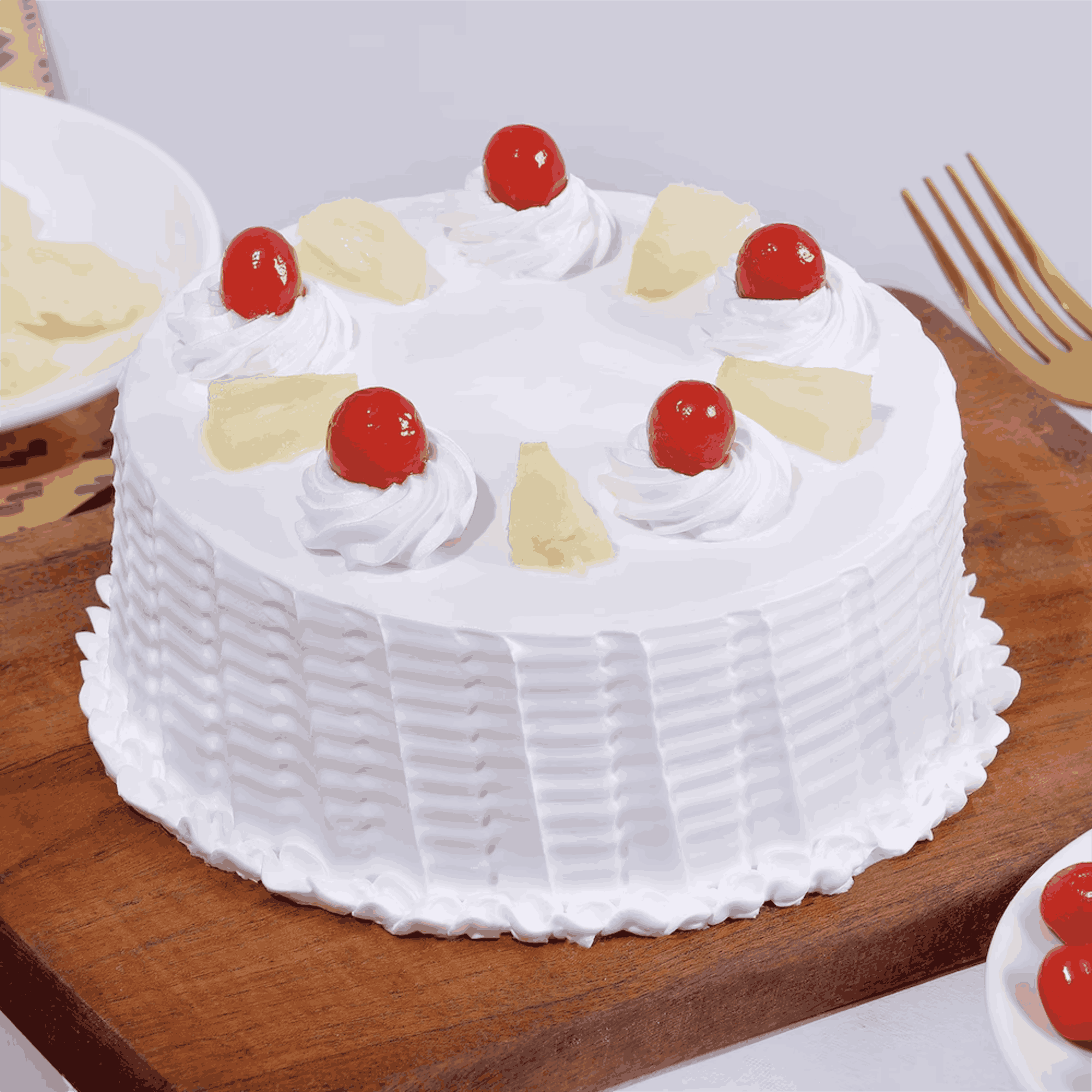 A round pineapple cake with white whipped cream layers and topped with cherries and pineapple segments, presented on a wooden board.
