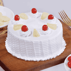 A round pineapple cake with white whipped cream layers and topped with cherries and pineapple segments, presented on a wooden board.