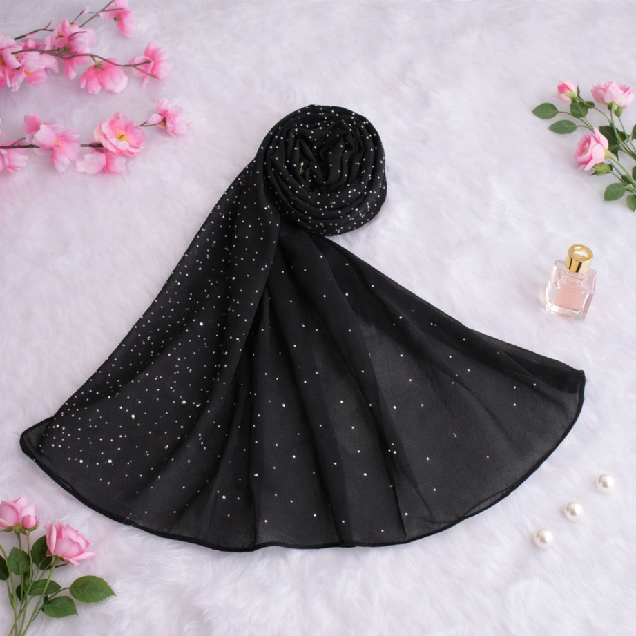 Rolled black studded hijab laid on a soft surface with floral decor, emphasizing its smooth chiffon fabric and premium modest fashion appeal.