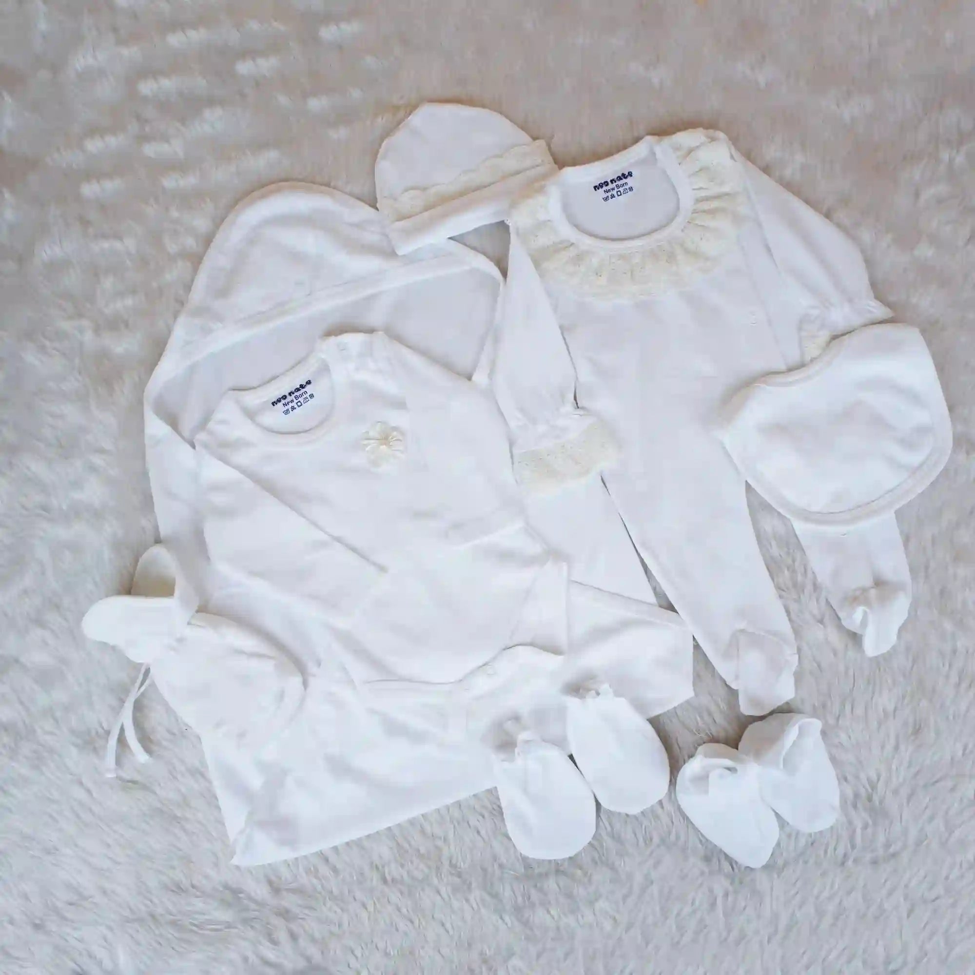 Collection of baby clothes including a onesie, pants, and socks on a textured surface