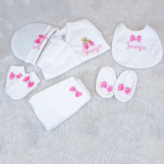 Baby clothing set with white bibs, hats, and socks featuring pink bows and embroidered names on a light gray background.