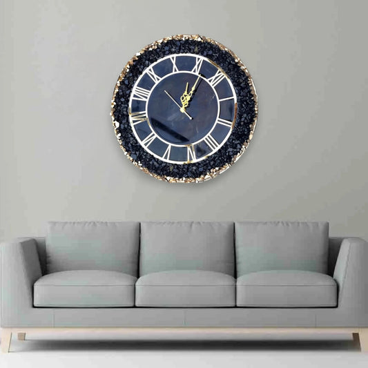 Black Grace Wall Clock with gold Roman numerals and crystal accents mounted above a grey sofa. Modern decor for luxury living rooms.