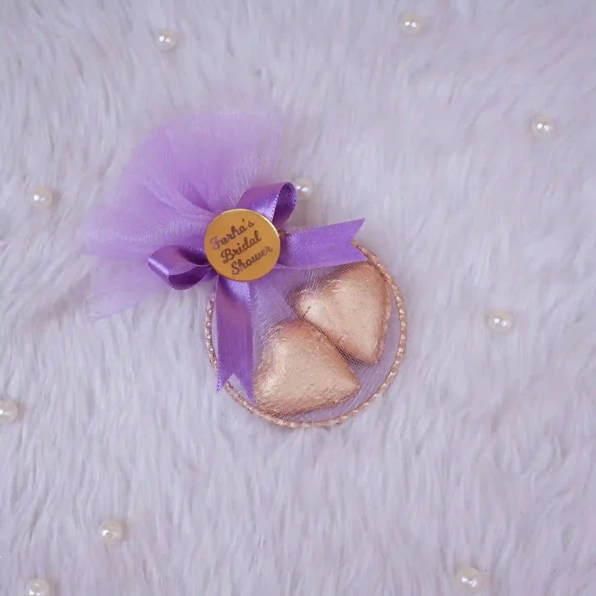 Decorative item with purple tulle, gold hearts, and a gold tag on a textured white background.