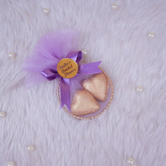 Decorative item with purple tulle, gold hearts, and a gold tag on a textured white background.