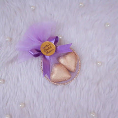 Decorative item with purple tulle, gold hearts, and a gold tag on a textured white background.