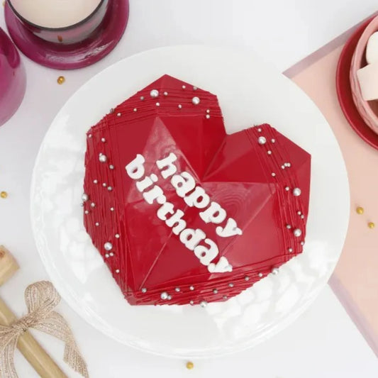 Red Velvet Pinata Cake in heart shape with 'Happy Birthday' text, decorated with silver pearls, ideal for surprise celebrations.