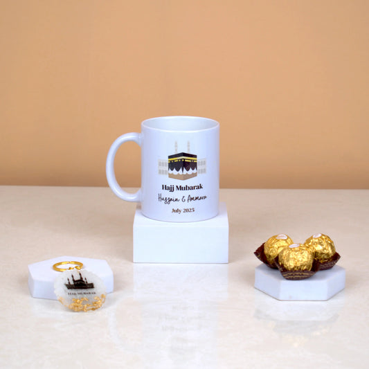 Barakah Blessings Hamper with Hajj Mubarak mug, Kaaba keychain, and chocolates on marble stands. Ideal Hajj souvenir gift set.