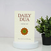 Book titled 'Daily Dua' with a decorative cover on a white surface next to a potted plant.