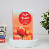 Book titled 'Daily Hadith' with a tulip design on a white surface with books and a plant in the background.