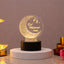 Illuminated acrylic LED lamp featuring a crescent moon with geometric patterns, hanging lanterns, and personalized "Eid Mubarak Saba" text, mounted on a round black base.