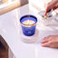 Ocean Mist Fragrance candle in a blue glass jar, lit on a white coaster, creating a refreshing scent with aquatic notes for home decor ambiance.