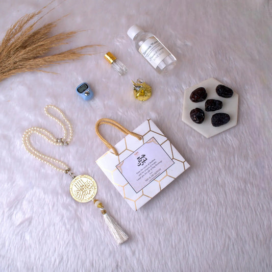 Barakah Hajj Gift Hamper Pack with tasbih, Zamzam water, Ajwa dates, and Islamic accessories on white fur background. Ideal Hajj return gift set.