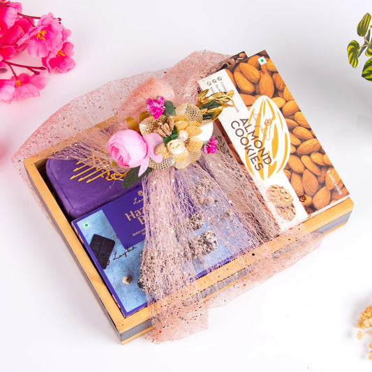 Velvet Bliss & Nut Hamper - Gourmet Delights gift set wrapped in pink netting, featuring premium nuts, cookies, and chocolates in a wooden box.