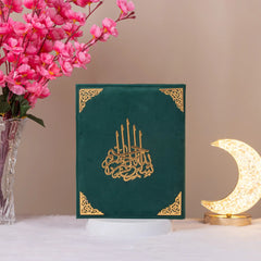 Velvet-covered Quran with golden Arabic calligraphy from Green Salah Combo Hamper, displayed upright with decorative elements.