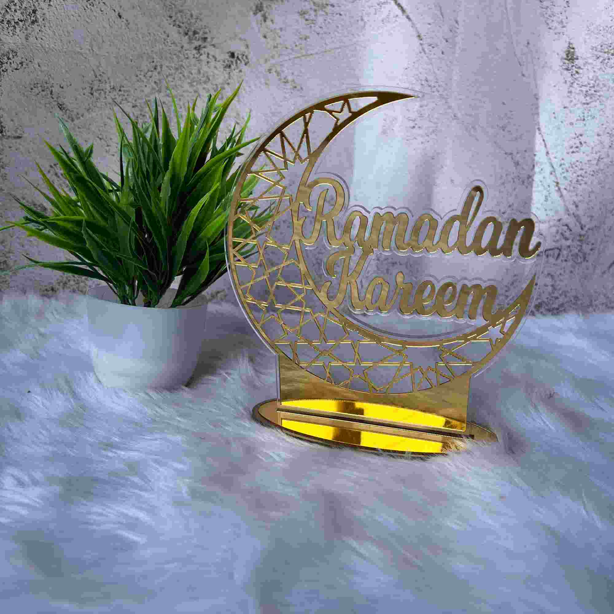 Ramadan Kareem Stand - Decorative Stand | Durable Design in gold with crescent moon shape, placed on white fur with green plant decor.