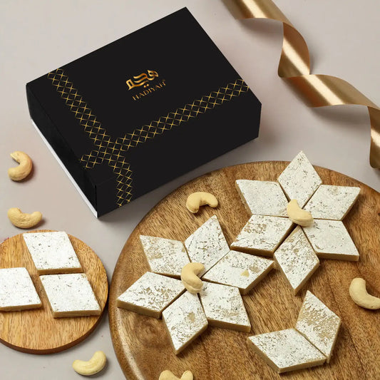 Premium Kaju Katli - Kaju Katli Online Buy | Pure Indian Sweets in elegant black gift box with silver-coated diamond-shaped sweets on wooden platter.