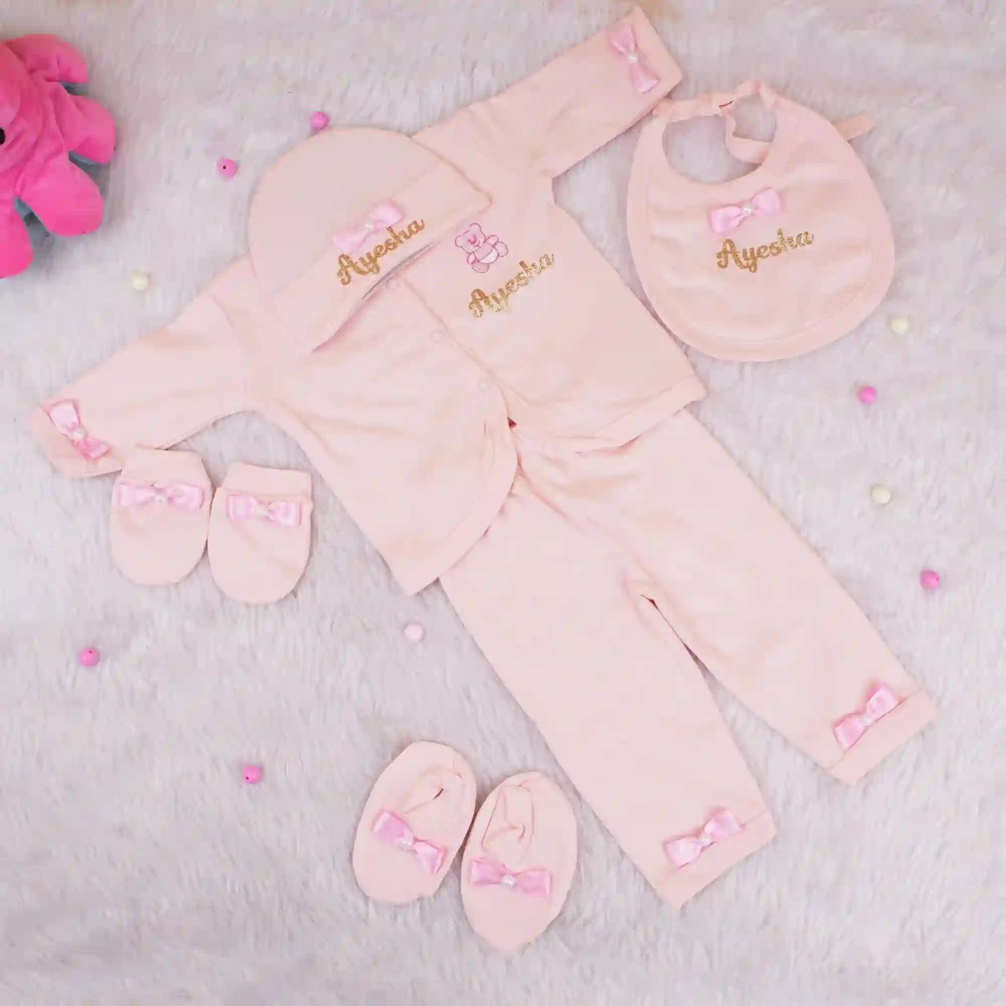 Pink baby outfit set with matching accessories on a light gray background
