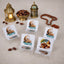 A collection of four small acrylic date stands arranged on a light-colored surface with scattered loose dates. Three of the stands feature a crescent moon and mosque design with "Ramadan Mubarak" text, while the fourth shows a printed design of a date bowl and lantern. The background includes two decorative Ramadan lanterns, a golden bowl of dates, and wooden prayer beads.