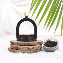 Midnight Crescent Bakhoor Burner with elegant black arch design and golden crescent top, placed on rustic wooden coasters beside bakhoor jar.