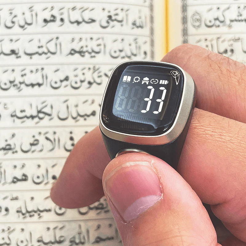 Noor Zikr Ring 2.0 in use during Quran reading, showing zikr count of 33 on digital screen for prayer tracking.