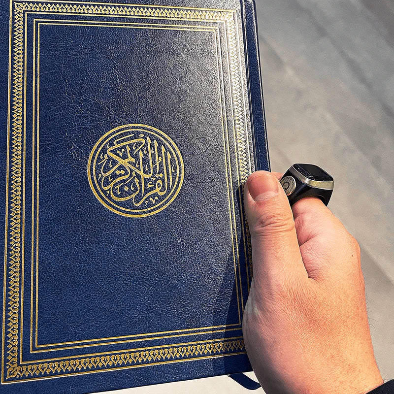 Hand holding Quran while wearing Noor Zikr Ring 2.0, combining digital zikr tracking with spiritual practice.