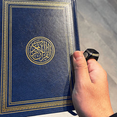 Hand holding Quran while wearing Noor Zikr Ring 2.0, combining digital zikr tracking with spiritual practice.