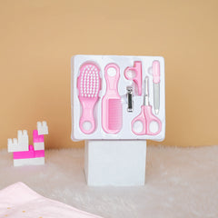 Set of pink grooming tools including a brush, comb, scissors, and clip in packaging on a beige surface.