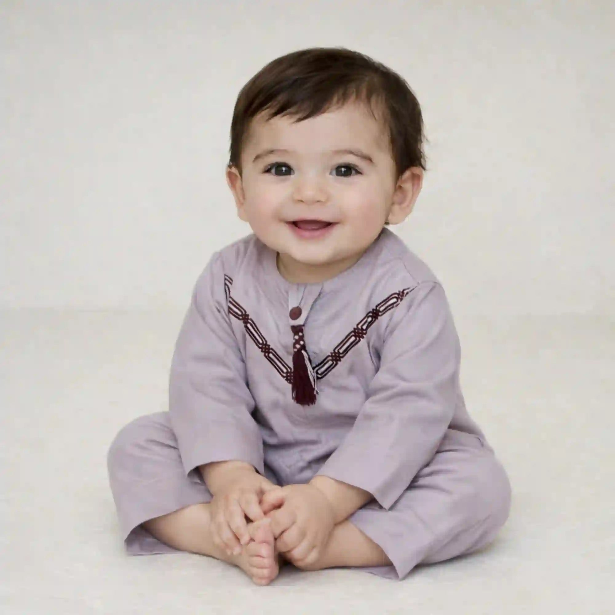 Smiling baby boy wearing a Purple Thobe Romper in soft Omani style, ideal for Ramadan and Eid celebrations. Perfect festive outfit from the Kids Collection.