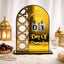 An arched gold acrylic Ramadan countdown calendar displaying the number 01 on hanging silver tiles above the text "Day Of Ramadan." The calendar features a cut-out geometric Islamic pattern on the left side and is displayed on a soft white surface alongside a bowl of dates, prayer beads, and gold lanterns.