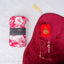 A red-themed Women's Namaz Essentials Hamper shown from above, including a rolled floral prayer dress, a red velvet prayer mat, a red mini velvet Quran box, matching red tasbeeh beads, and a digital counter.