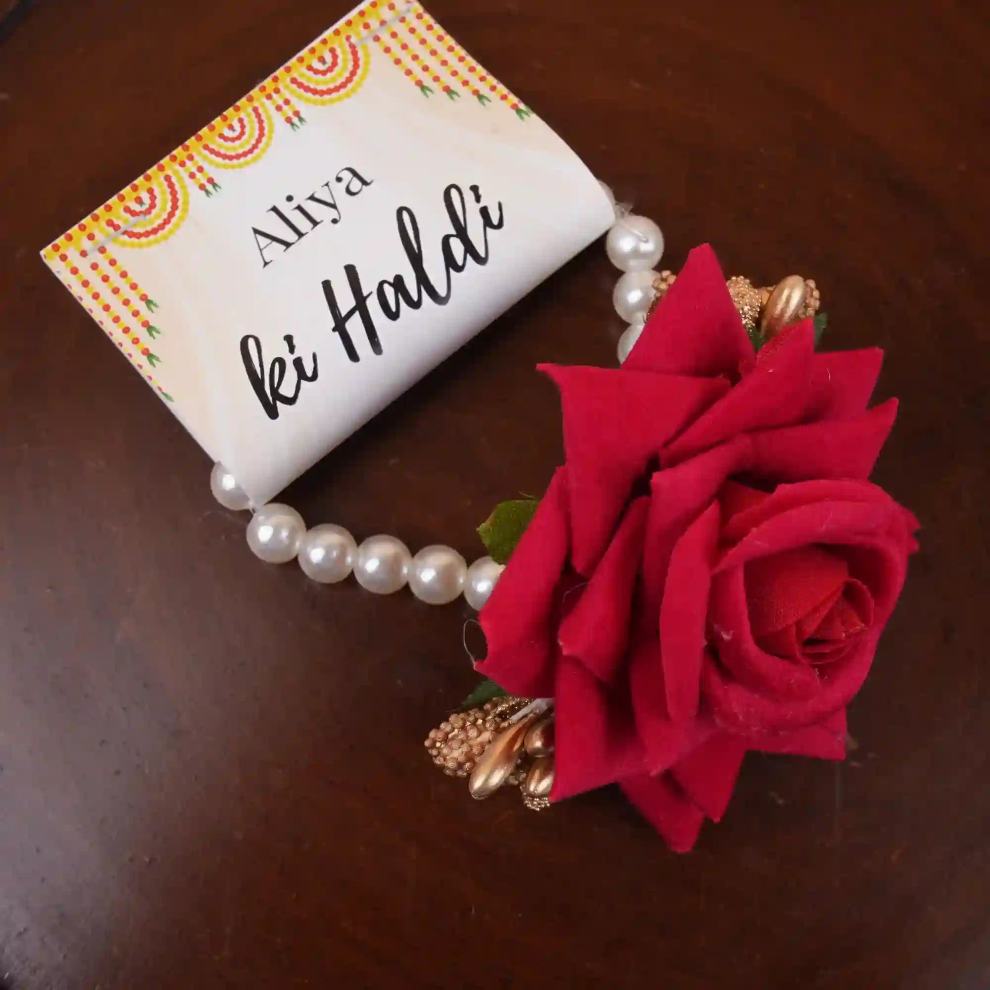 Bracelet with red rose and pearl beads on a card with 'Aliya ki Haldi' text.