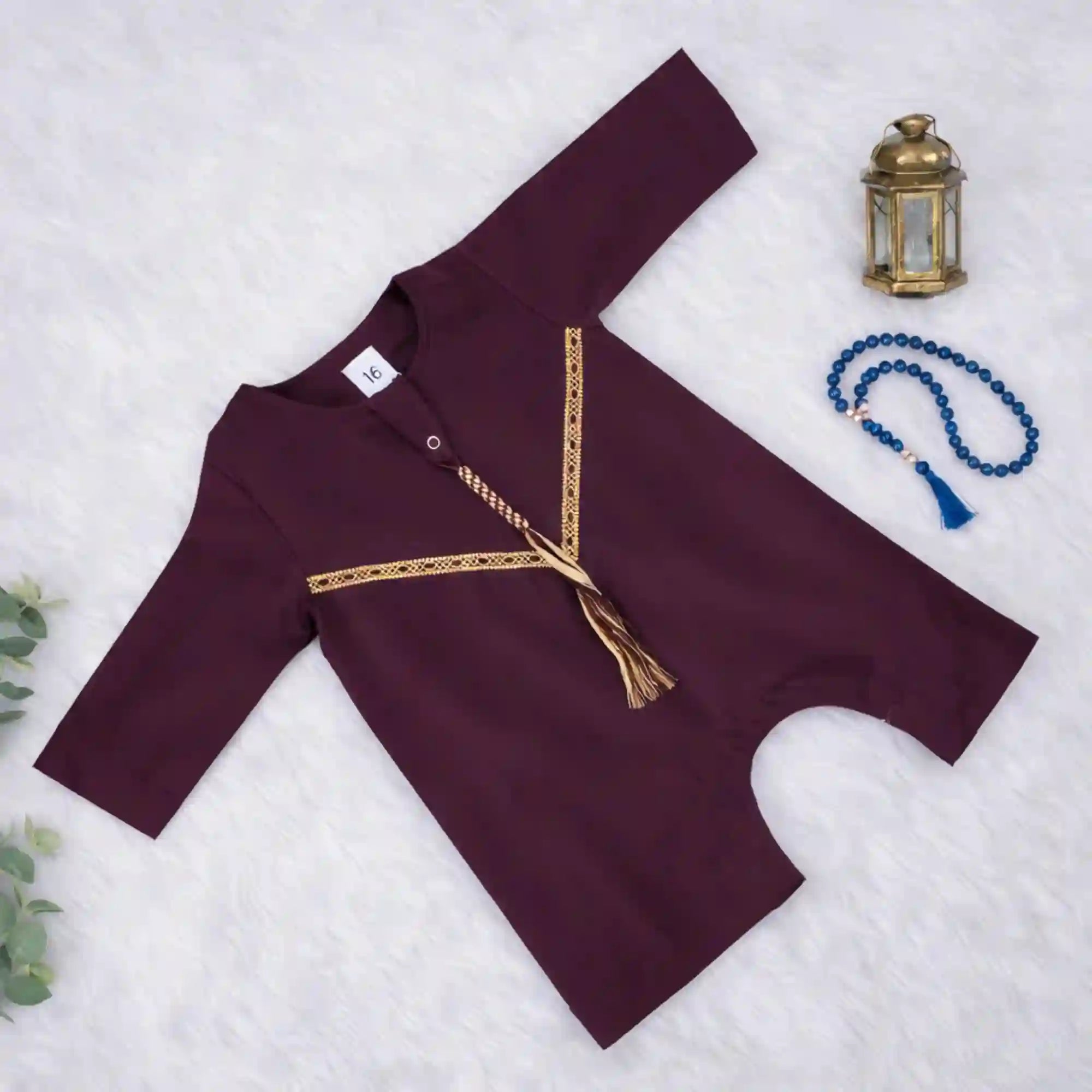 Flat lay of maroon thobe romper for baby boys featuring gold Omani style trim, soft fabric, and easy snaps for diaper changes.