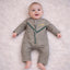 Close-up of baby boy in beige traditional outfit with embroidered details, lying on soft white surface