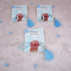 Three blue Little Hands Tasbeeh Keepsakes with name 'Taimur' on soft pink background, perfect for religious Aqiqah favors.