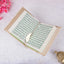 Open book with green text on a white surface with pink flowers