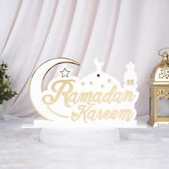 Decorative sign with 'Ramadan Kareem' text on a white background with a gold lantern and green plant.