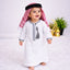 Baby boy wearing traditional white thobe with embroidery, standing on white fluffy rug