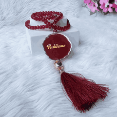 Personalized red tasbeeh with golden name tag and tassel, featured in Amaanat-e-Nikaah Maroon Bling Collection for bridal gifts.