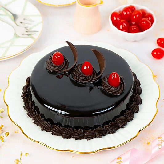 Yummylicious Chocolate Cake - Order Dessert Online | Rich Indulgence, glossy round chocolate cake topped with cherries and chocolate swirls on a white plate.
