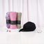 Front display of the Modest Style Set Women's Hamper contents on a white surface. Three rolled hijabs in purple floral, pink, and olive green stand upright on a small display riser, next to a black hijab cap, a diamond pin, a hijab magnet, and a wheel of colorful pins.