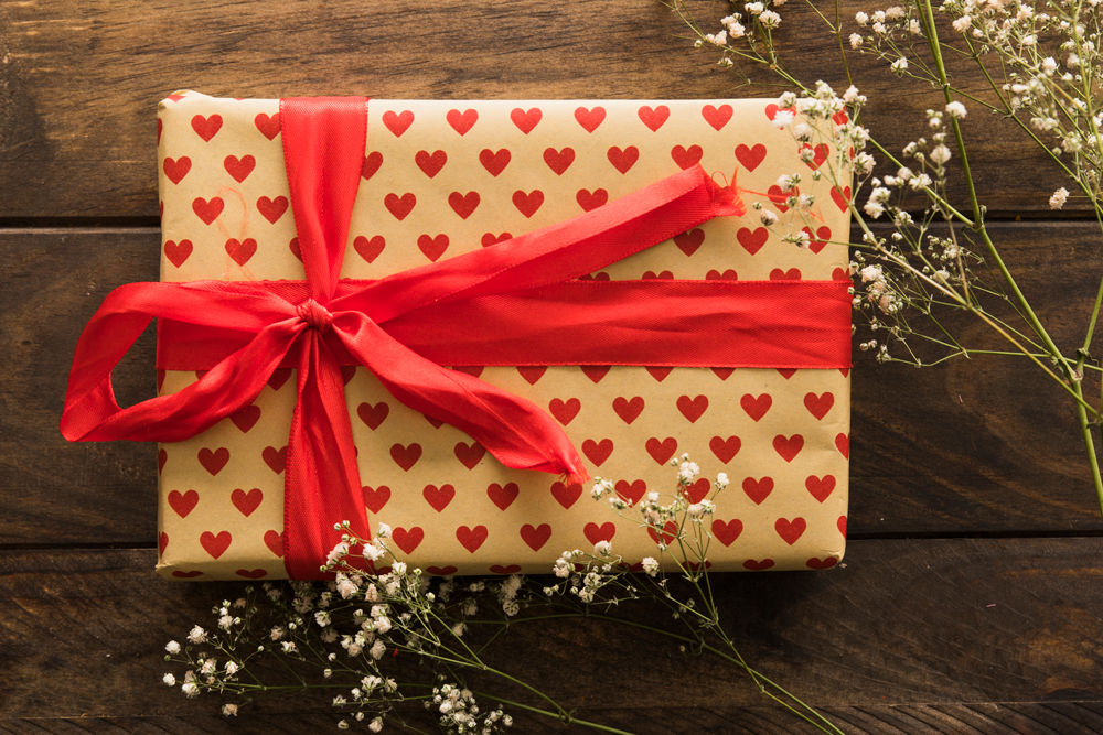Ramadan gift wrapped in heart-patterned paper with red ribbon on wood.