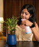 Woman watering a plant with a pink spray bottle in a warm indoor setting