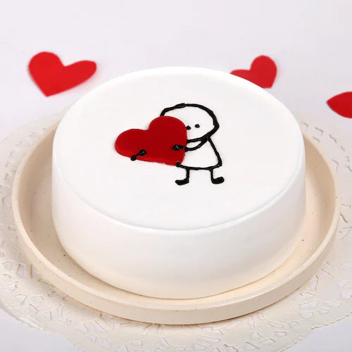 Vanilla Heart Cake featuring adorable character hugging red heart, ideal for romantic occasions. Smooth white frosting and round shape design.