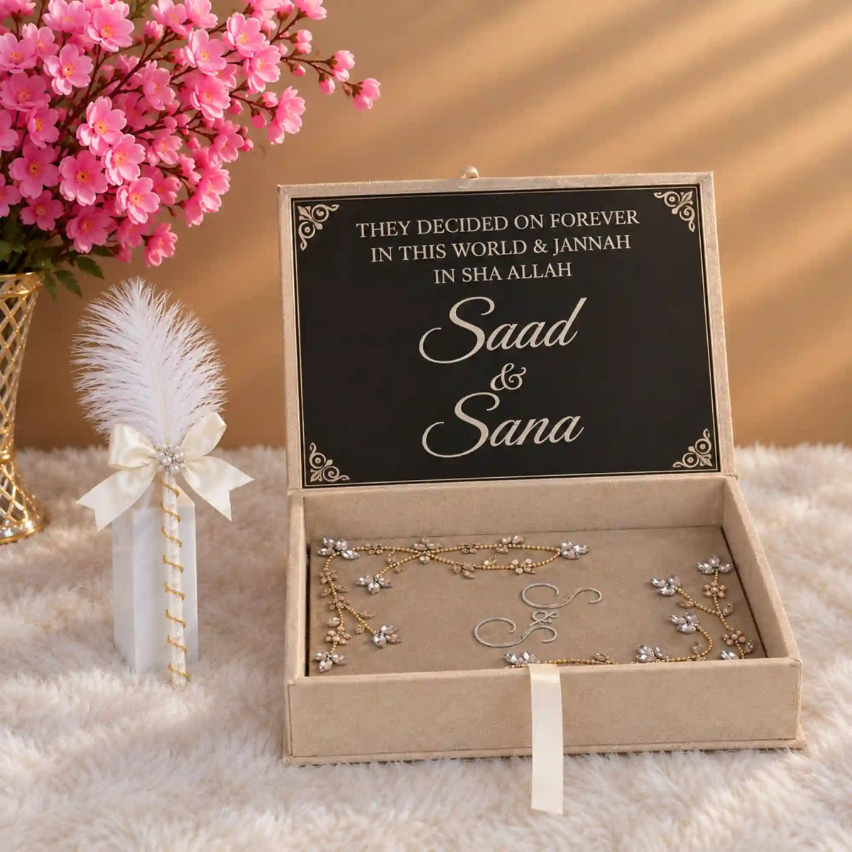 A personalized jewelry box with a black sign inside reading 'THEY DECIDED ON FOREVER IN THIS WORLD & JANNAH IN SHA ALLAH Saad & Sana' in elegant white script. The open beige box contains delicate gold and silver floral jewelry.