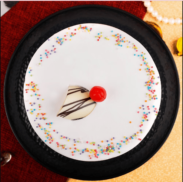 Top view of Vanilla Cake - Moist Delight featuring smooth whipped cream frosting, colorful sprinkles, and cherry garnish, perfect for celebrations.