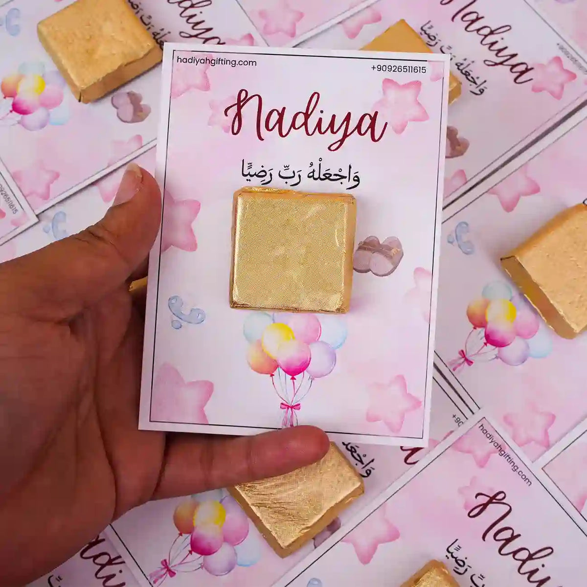 Hand holding Aqiqah Sweet Blessings Favor with gold chocolate and custom pink card labeled 'Nadiya', perfect for Aqiqah party giveaways.