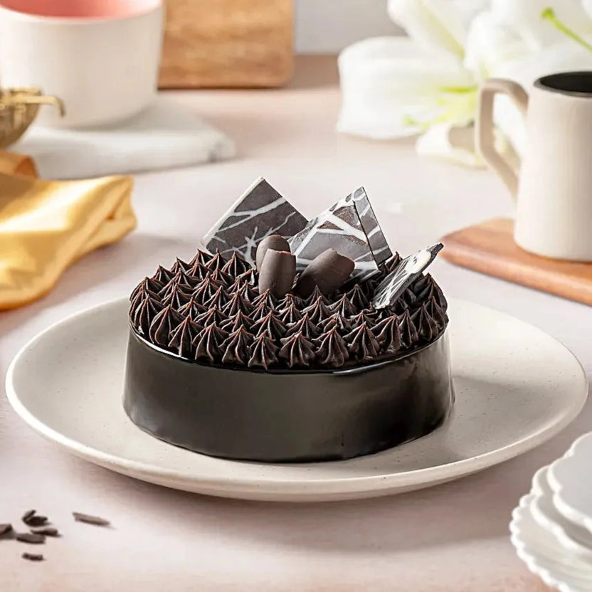 Fudge Brownie Cake with rich chocolate fudge topping and decorative chocolate shards on a white plate. Ideal for same day delivery chocolate cake gifts. Main image