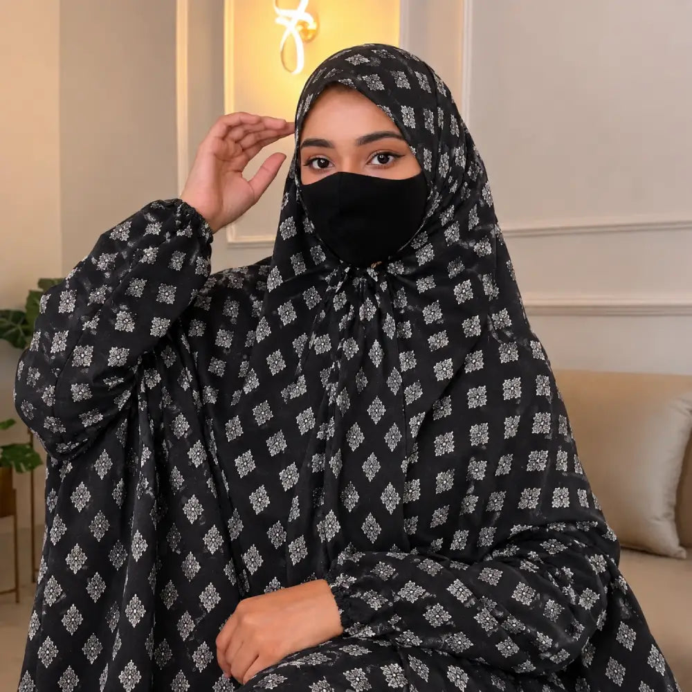 Woman wearing a black and white patterned abaya with a matching face mask indoors.