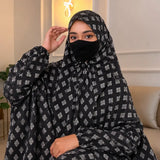 Woman wearing a black and white patterned abaya with a matching face mask indoors.