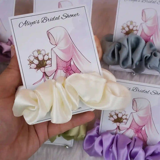 Cream satin scrunchie on personalized bridal shower card featuring elegant hijabi bride illustration, perfect for wedding favors.